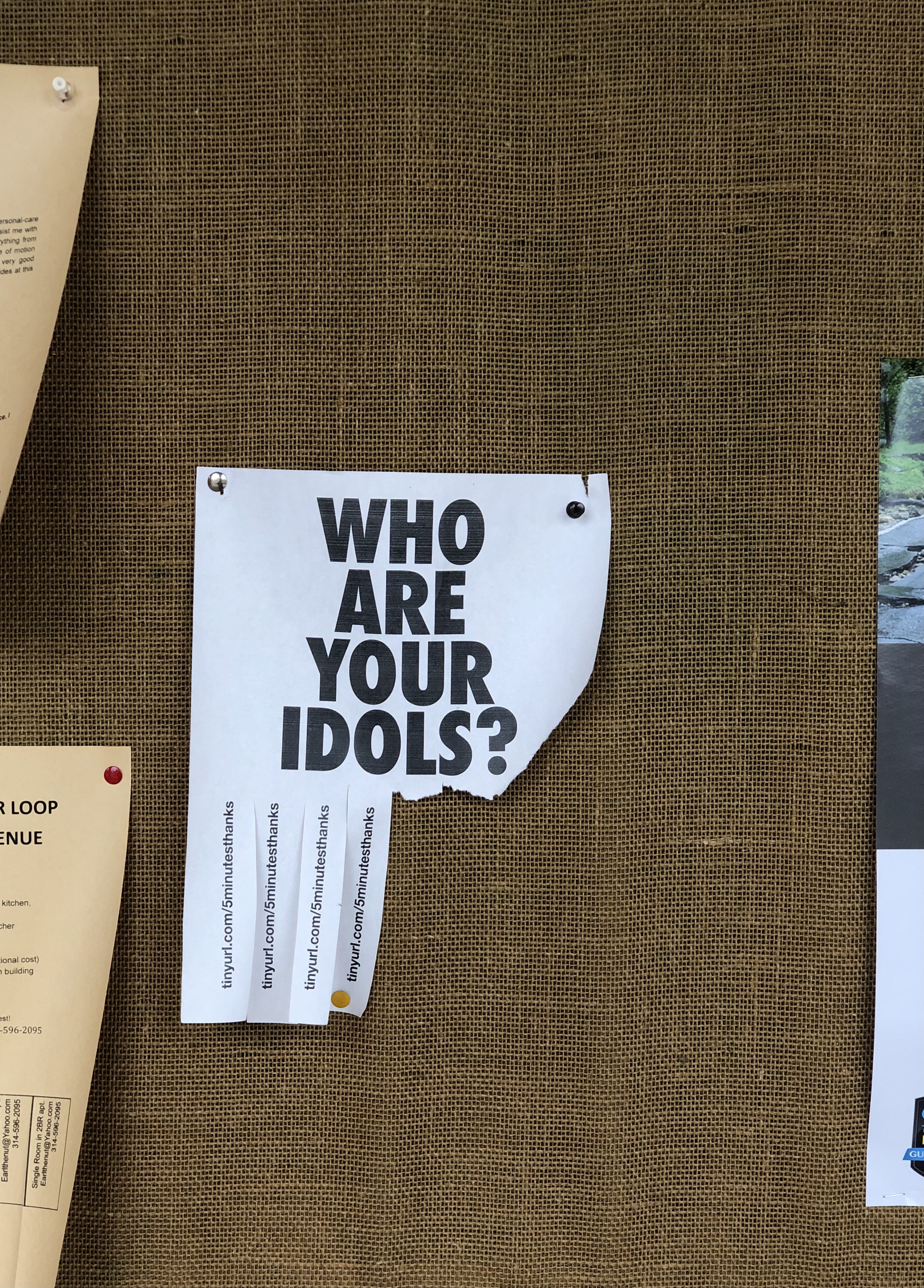a flyer with text 'WHO ARE YOU IDOLS?'' in a bold, black font in the center, pinned to a board.