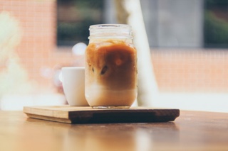 Mason jar with coffee, ice cubes and milk, next to a white coffee cup