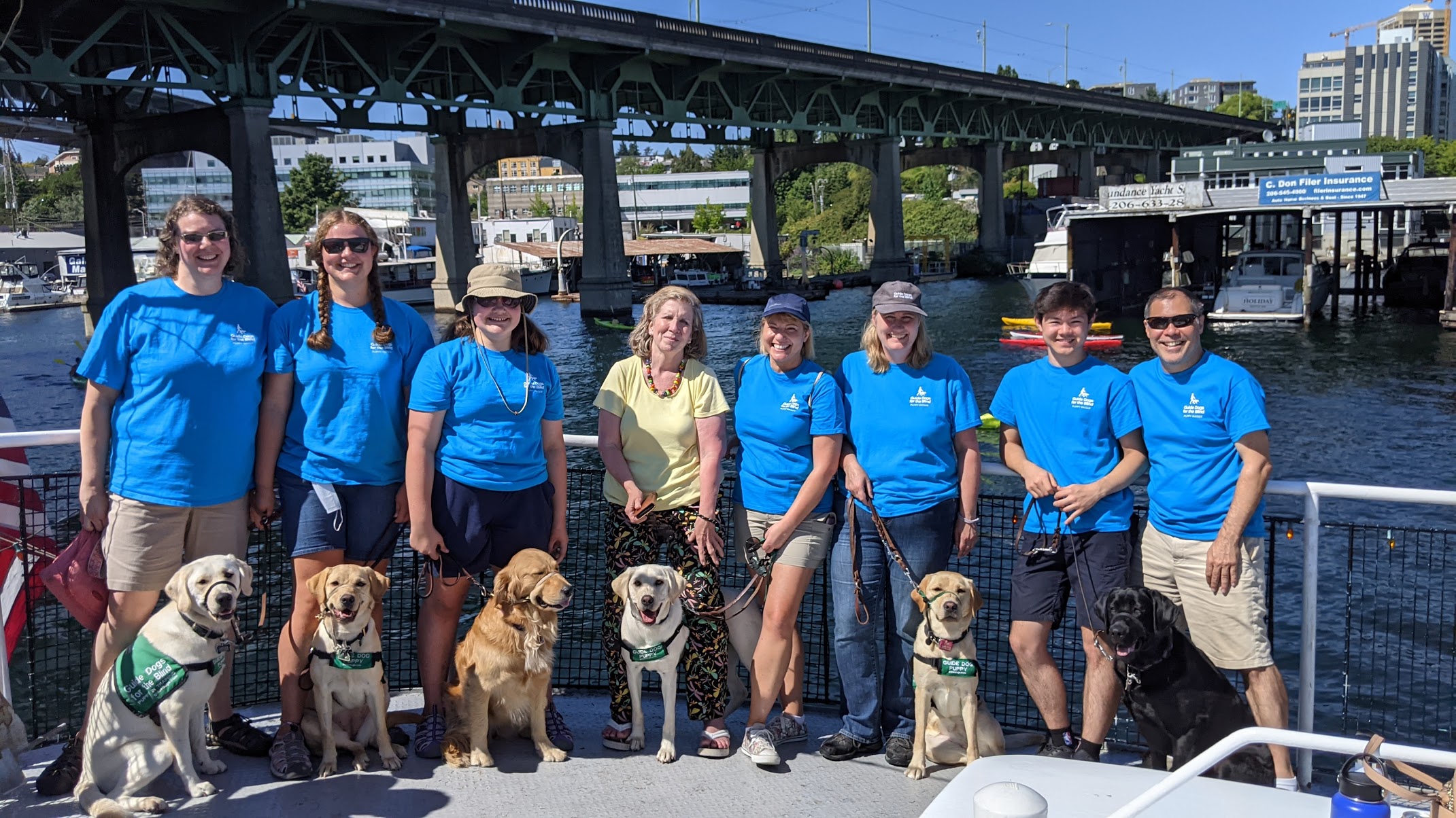 GDB Bellevue Puppy Club outing on a boat. Puppy raisers lined up with puppies in training sitting next to them facing camera.